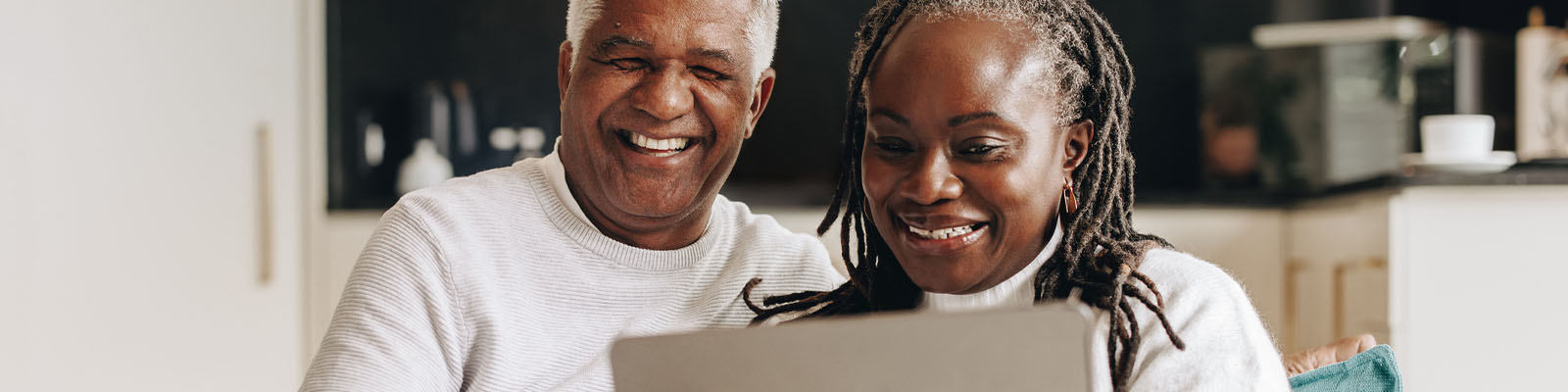 A senior man and woman sitting together on a couch looking down at a laptop